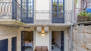 Ein zweigeschossiges Gebäude mit Balkon, Bank und einer kleinen Eingangszone mit Tür und Fenster.