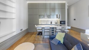 Eine moderne Küche mit einer zentralen Kochinsel, Barhocker und einem grauen Sofa mit Zierkissen.