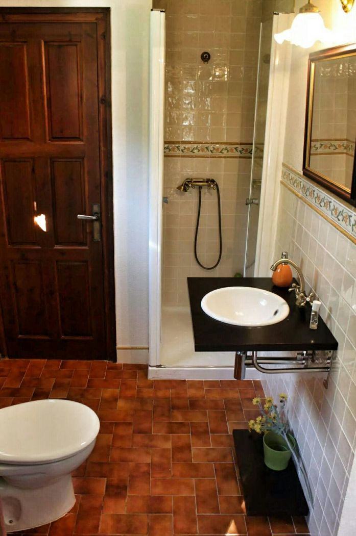 A bathroom with a wooden door, a white toilet, a sink with a black countertop, a shower with a glass door, and a mirror with a gold frame.