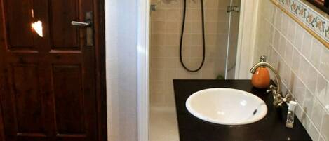 A bathroom with a wooden door, a white toilet, a sink with a black countertop, a shower with a glass door, and a mirror with a gold frame.