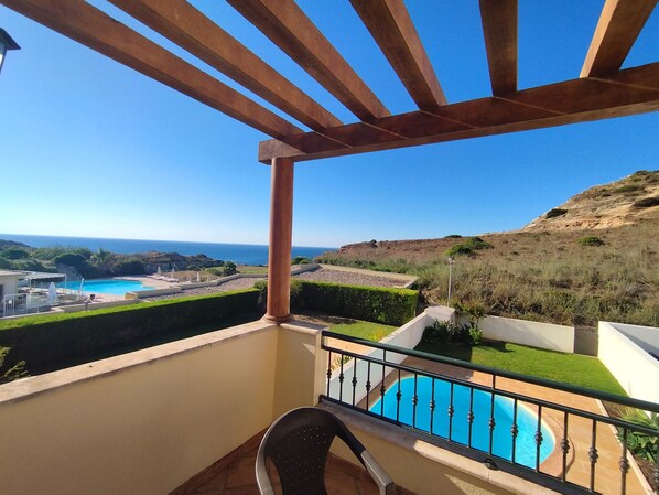 Varanda com vista para uma piscina e o mar.