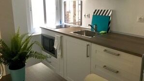 A compact kitchen with a sink, cabinets, a window, and a potted plant.