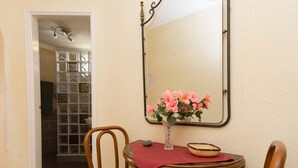 A dining area with a table, chairs, a vase with flowers, a mirror, and a door leading to a bathroom. - Santa Maria 88 - Two Bed (Costa Adeje)