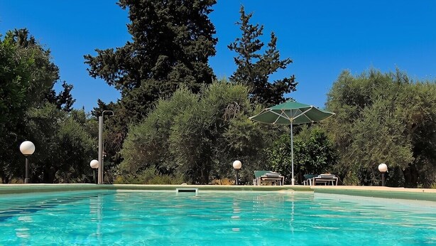 A clear swimming pool surrounded by trees, with a gazebo and lounge chairs in the background. - A Recently Refurbed 3 Bedrm Villa, Large Pool, Great Privacy, Close to Amenities (Chania)