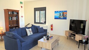 A living room with a blue sofa, a coffee table, a bookshelf, a television, and a painting on the wall. - A Recently Refurbed 3 Bedrm Villa, Large Pool, Great Privacy, Close to Amenities (Chania)