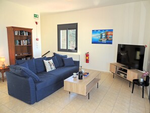 A living room with a blue sofa, a coffee table, a bookshelf, a television, and a painting on the wall.