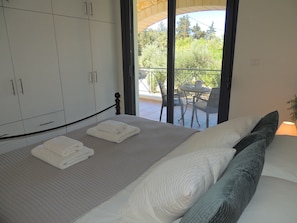 A bedroom with a bed, a wardrobe, and a balcony with a table and chairs.