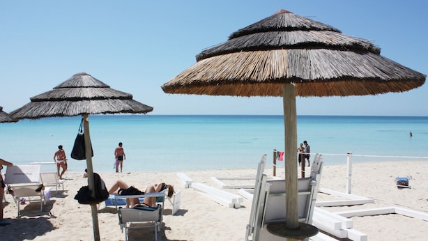 Une plage avec des parasols en chaume, des chaises longues et une vue dégagée sur l’océan.