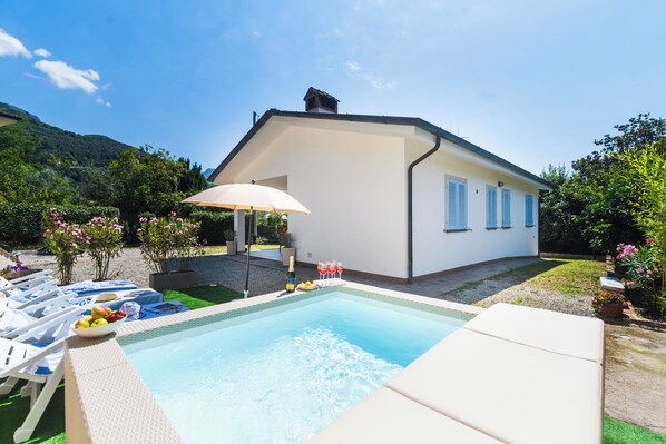 A swimming pool with lounge chairs, a table with drinks, and a house with a garden. - Comfortable new villa, quiet and relaxing Tuscan countryside, nature, sun, sea (Camaiore)