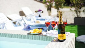 A bottle of Valdo wine, two glasses of red wine, and a plate of lemon slices on a table by a poolside lounge area. - Comfortable new villa, quiet and relaxing Tuscan countryside, nature, sun, sea (Camaiore)