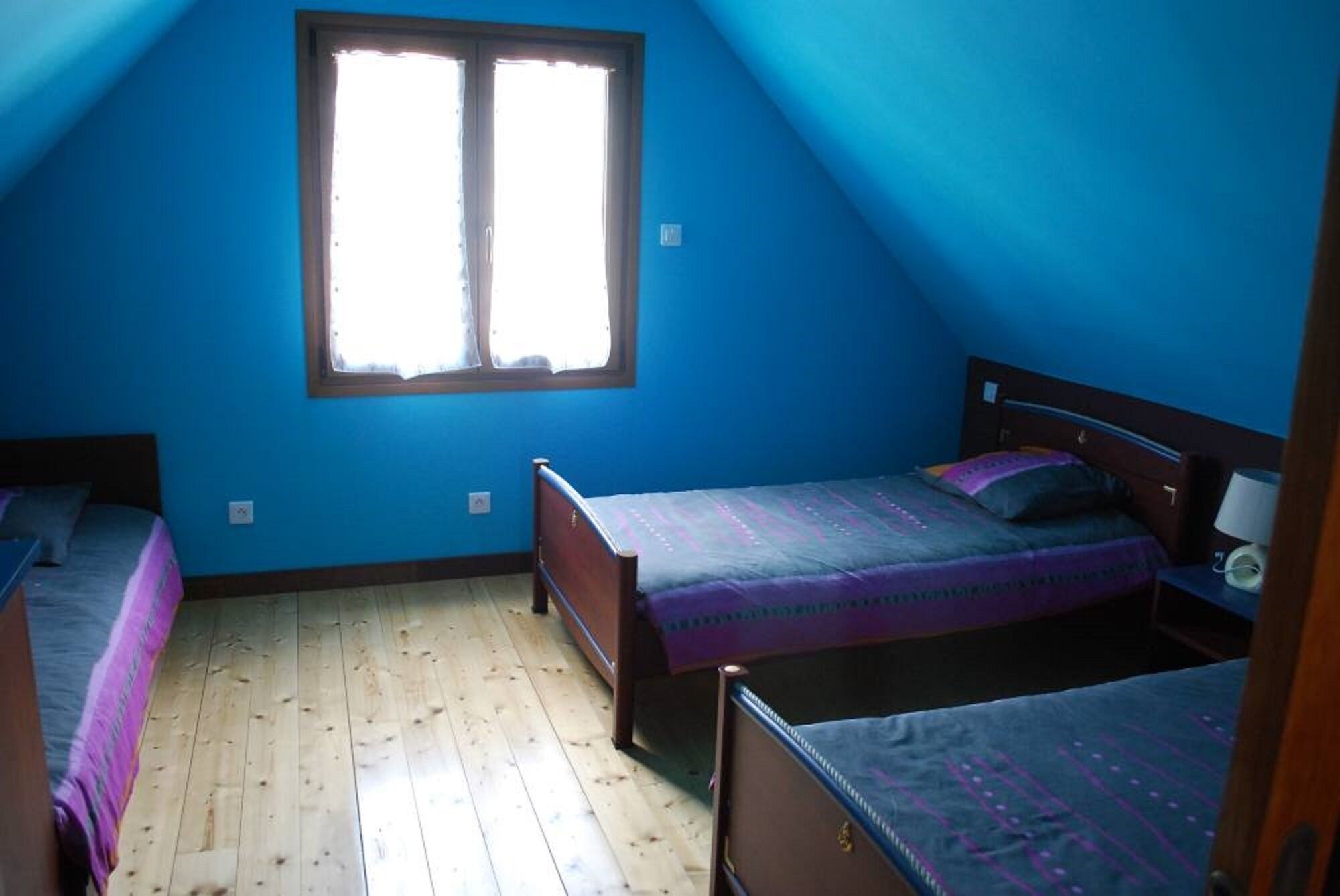 A room with two beds, a window, and a wooden floor.