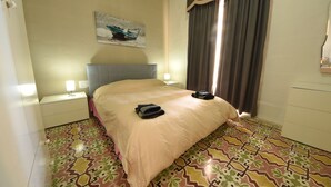 Una habitación de hotel con una cama, una mesita de noche, una lámpara, un cuadro en la pared y baldosas con diseño en el suelo.