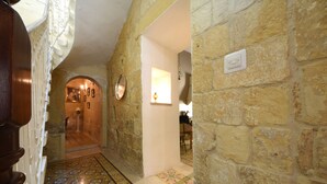 Un pasillo de paredes de piedra con piso estampado, una puerta con espejo y un interruptor de luz en la pared.
