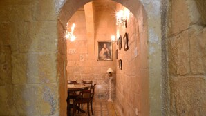 Un comedor con paredes de piedra, una mesa redonda y sillas, un candelabro y un cuadro en la pared.
