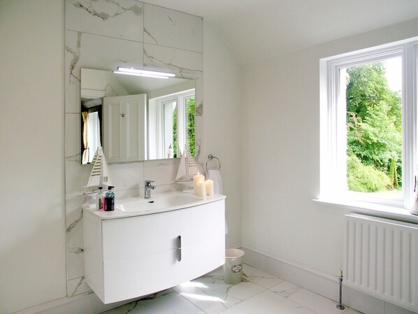 Ein modernes Badezimmer mit einem weißen Waschtisch, einem großen Spiegel und einem Fenster mit Blick auf Grünflächen.