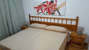 Un dormitorio con cabecera de madera, dos mesitas de noche con lámparas, una cama con colcha a cuadros y un cuadro de flores en la pared.