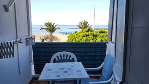 Un balcón con vista a la playa, una mesa y dos sillas.