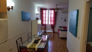 Un comedor con una mesa de vidrio, sillas y una disposición tipo bufé. Se observa un sofá y un ventilador de techo al fondo.