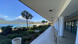 A covered walkway with a view of the sea, a beach, and mountains in the background.