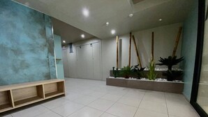 A spacious lobby with a wooden bench, a tiled floor, a wall-mounted planter with plants, and a ceiling with recessed lighting.
