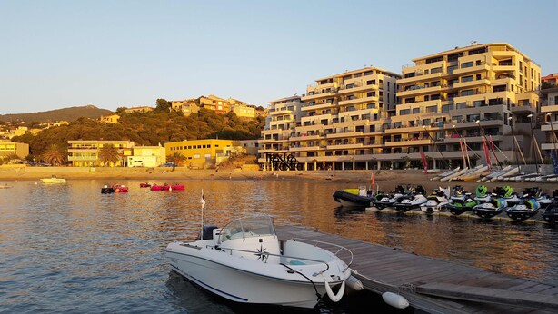 A marina with boats docked, a wooden pier, and a backdrop of multi-story buildings.