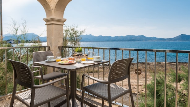 Una terraza con una mesa dispuesta para el desayuno, con vistas a un cuerpo de agua y montañas.
