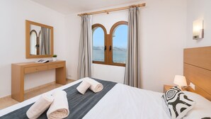 Una habitación de hotel con cama, escritorio de madera, espejo, mesita de noche con lámpara y ventana con cortinas.