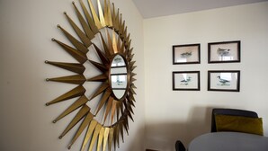 A room with a sunburst mirror, framed artwork, and a bed with a green pillow.