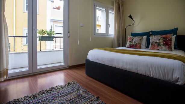 A bedroom with a bed, a window, a balcony, and a plant.