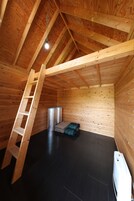 Un dormitorio abuhardillado de madera con una escalera, un calentador y una pila de mantas dobladas.