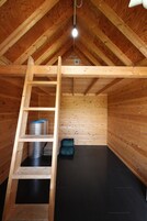 Uma cabana de madeira com um mezanino, uma escada e piso preto.