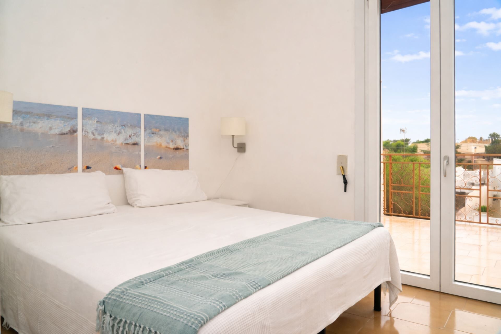 Ein Schlafzimmer mit Bett, Meerblick durch eine Glastür und einem Balkon mit Geländer.