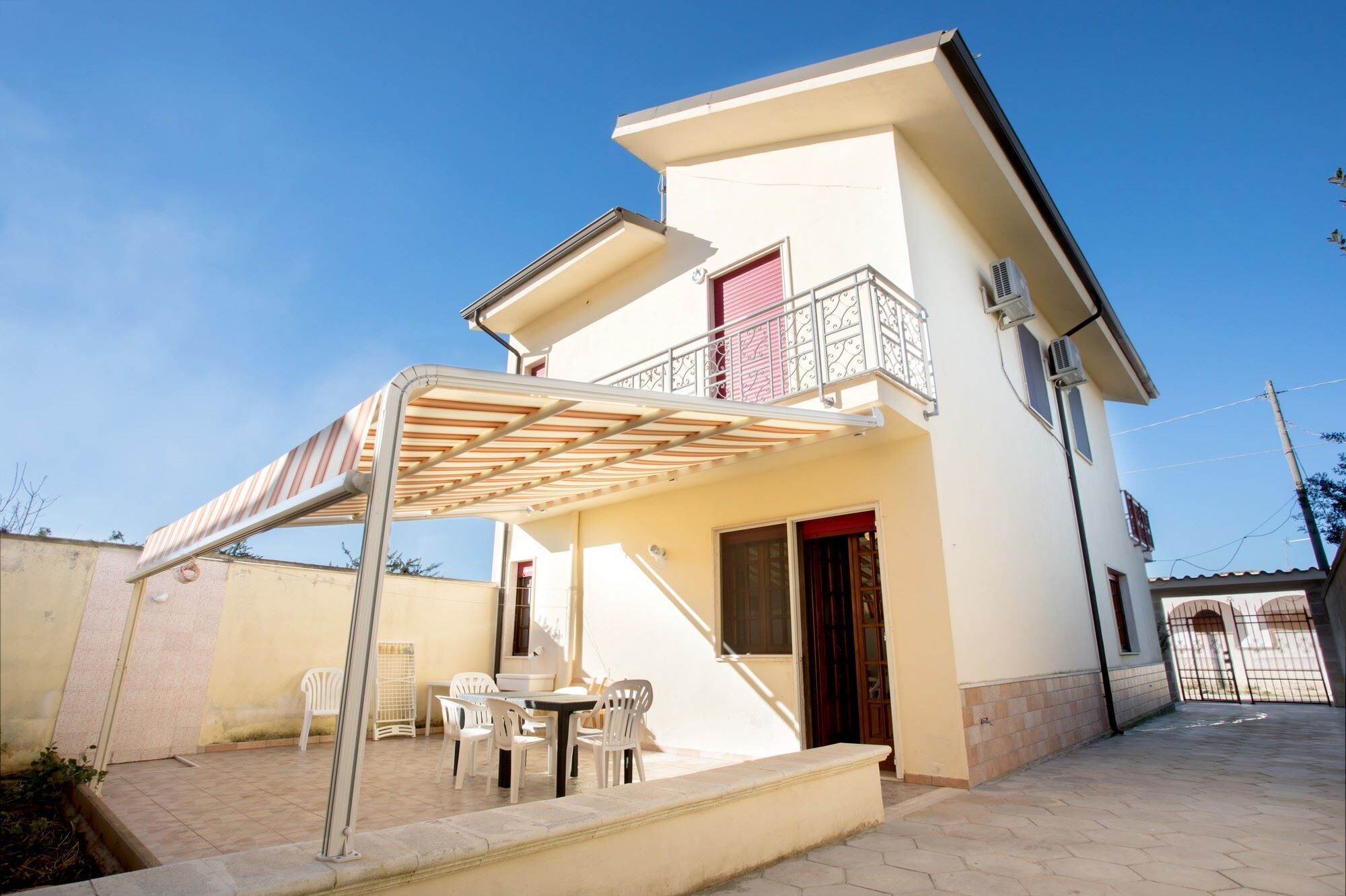 Una casa a due piani con una veranda coperta, un balcone e un piccolo spazio esterno arredato con sedie e un tavolo.