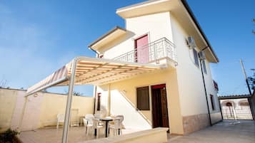 Una casa a due piani con una veranda coperta, un balcone e un piccolo spazio esterno arredato con sedie e un tavolo.