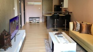 Un salon moderne avec un canapé, une table basse et un téléviseur. Il y a également un coin cuisine avec un comptoir et des tabourets.