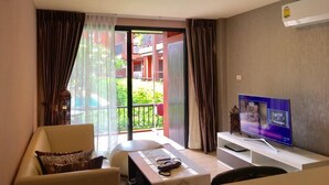 Un salon moderne avec un canapé, une table basse et un téléviseur à écran plat posé sur un meuble. Une porte-fenêtre coulissante donne accès à un balcon extérieur.