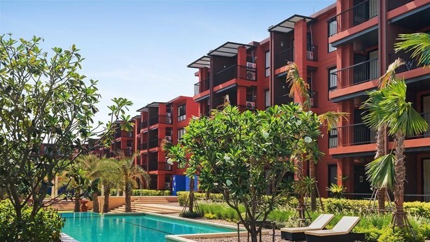 Une piscine entourée d’une végétation luxuriante et de bâtiments rouges dotés de balcons.