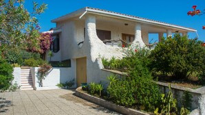 A white building with a tiled roof, a balcony, and a staircase leading to the entrance. - Veranda Piau  (Tertenia)