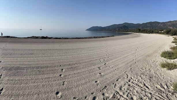 A beach with a clear sky, a boat in the distance, and mountains in the background. - Veranda Piau  (Tertenia)