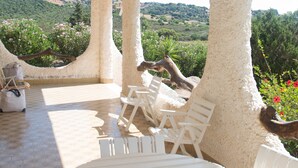 A covered outdoor seating area with a table and chairs, a lamp, and a view of a hillside. - Veranda Piau  (Tertenia)