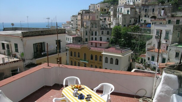 A terrace with a table and chairs, a view of a coastal cityscape, and a building with 'ENRICO PROTO' signage. - ATRANI "Pompeo" AMALFI COAST (ATRANI)