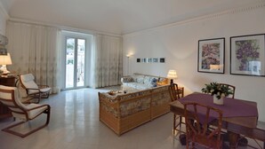 A spacious living room with a sofa, chairs, a dining table, and a view through a large window. - ATRANI "Pompeo" AMALFI COAST (ATRANI)