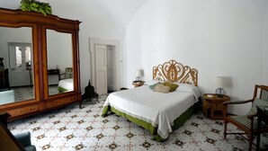 A bedroom with a large mirror, a bed with a green bedspread, a chair, and a small table with a lamp. - ATRANI "Pompeo" AMALFI COAST (ATRANI)