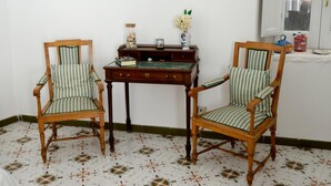 Two wooden chairs with striped upholstery, a small wooden table with a green marble top, and a vase with white flowers on a white wall. - ATRANI "Pompeo" AMALFI COAST (ATRANI)