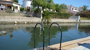 Piscina con barandillas metálicas, rodeada por un muro de piedra y una valla.