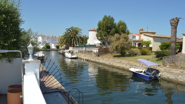 Un canal con barcos, un edificio blanco con techo rojo y una palmera.