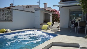Un jacuzzi con borde de azulejos, rodeado de sillones de descanso y un patio con mesa y sillas.