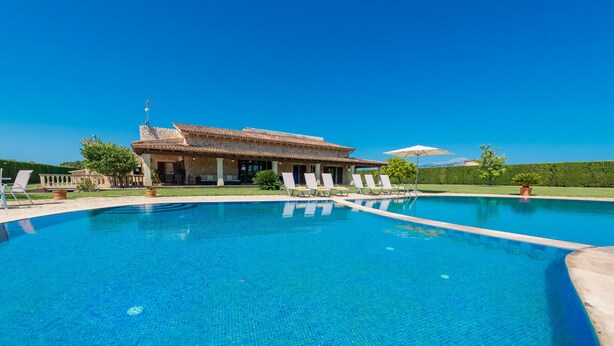 A large swimming pool with lounge chairs and a building with a tiled roof in the background.