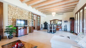 A spacious living room with a stone wall, a television, a dining area, and a white sofa.