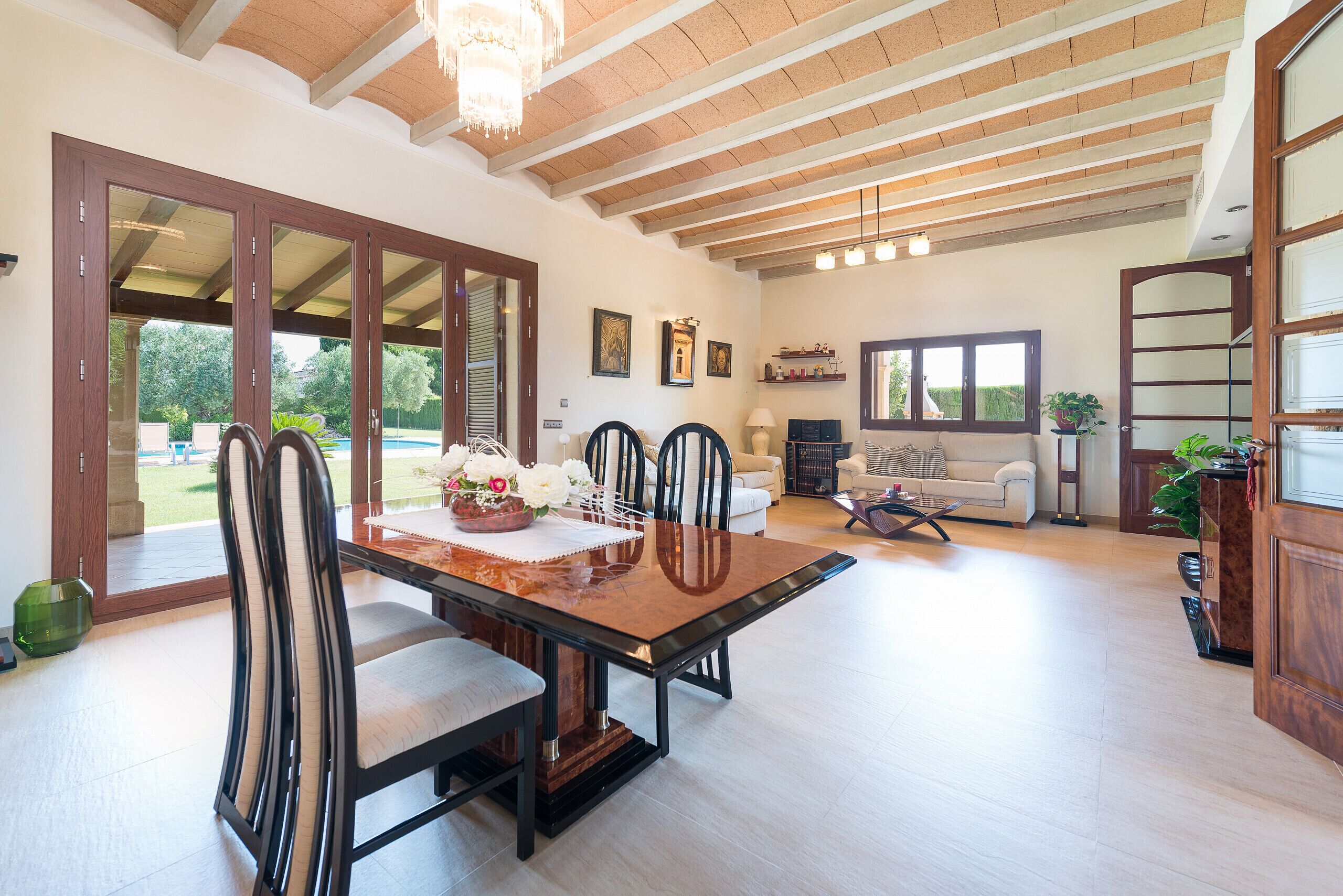 A spacious living area with a dining table, chairs, and a sofa. There are large windows and a view of the outdoors.